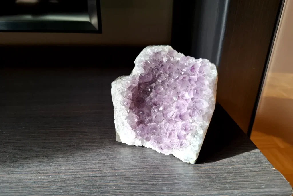 Amethyst cluster with pale purple points sitting in sunlight on a dark wood shelf