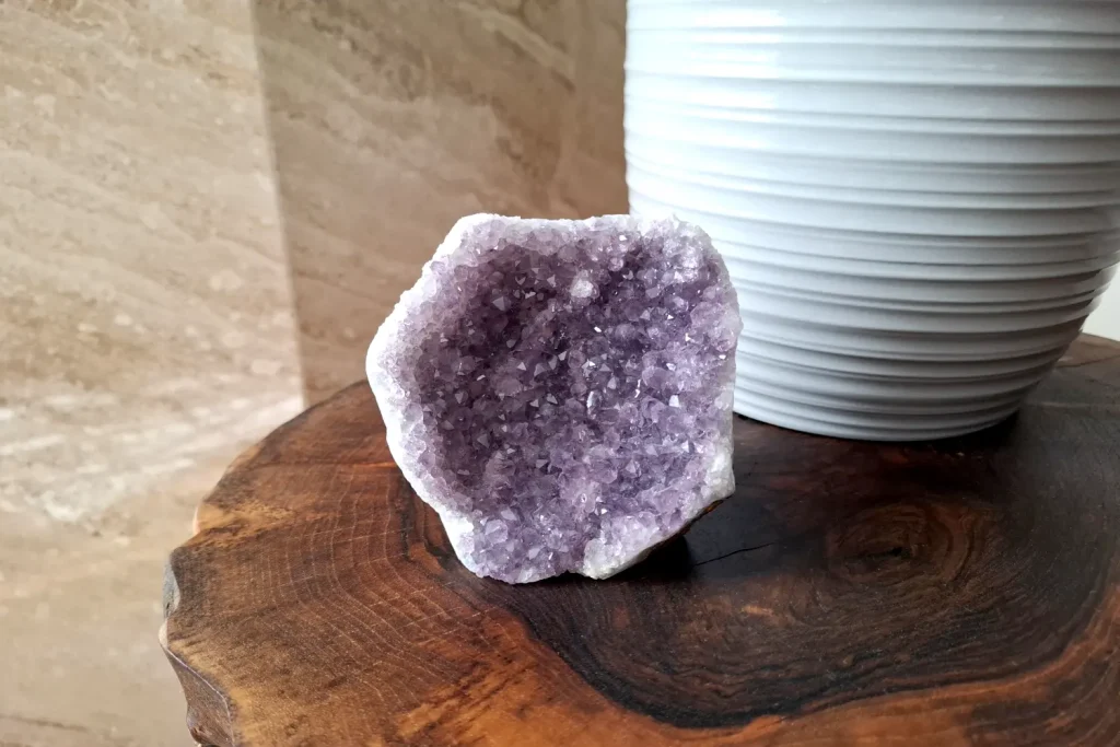 Amethyst cluster on a wooden table beside a white vase.