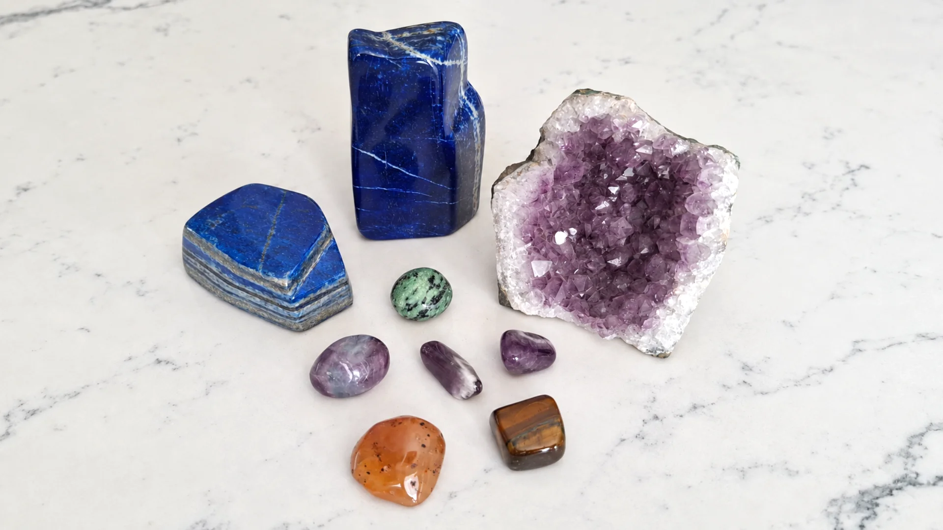 Amethyst geode beside polished blue stones and colorful tumbled crystals.