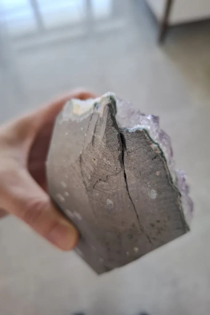 Hand holding the grey rock back of an amethyst cluster, with a crack running down the middle