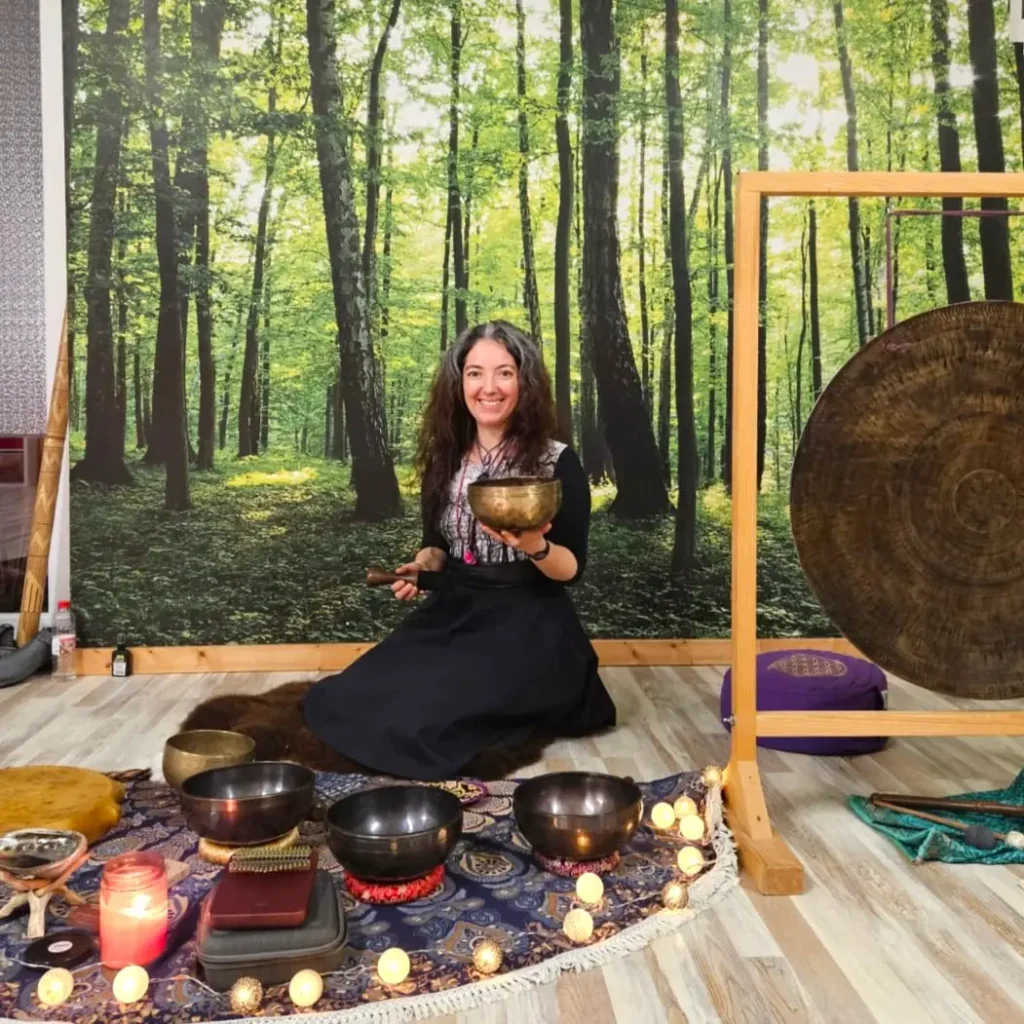 Darija Huzimec smiling, seated on a round rug among singing bowls and holding one, with a large gong beside her
