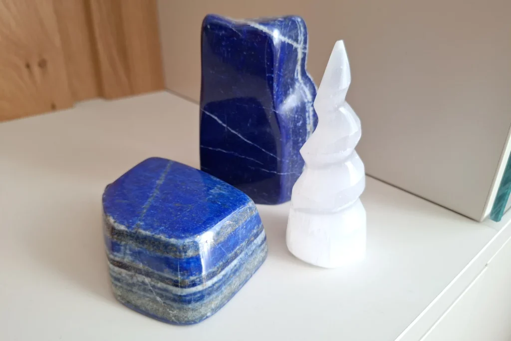 Two polished lapis lazuli pieces beside a white selenite tower on a shelf.