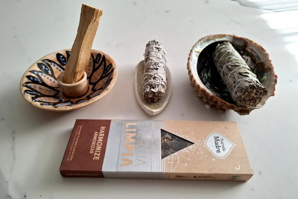 Two sage bundles, a wood stick in a ceramic holder and a Sagrada Madre incense box labeled Harmonize and Energía Limpia
