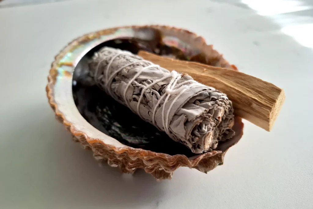 Unlit sage bundle and a wood stick resting in an abalone shell